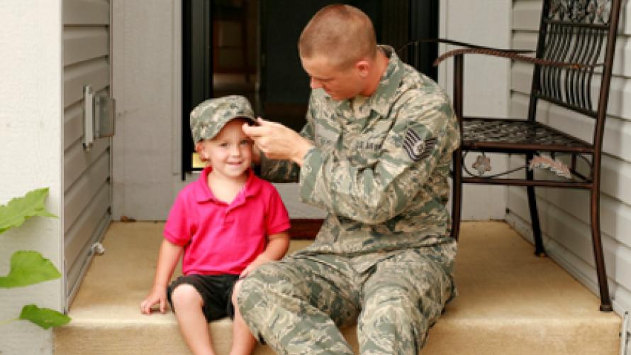 Military father putting his hat on his child